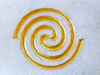 Die Doppelspirale (hier mit Blattgold auf weißem Marmor) ist ein Symbol für das Werden und Vergehen. Foto (C) Irmgard Brottrager